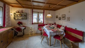 Un coin repas avec une table en bois dressée pour quatre personnes, des bancs recouverts d’un tissu rouge et un petit sapin de Noël.