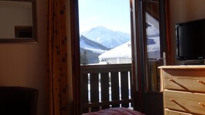 Une chambre à coucher comprenant un lit, une commode, un téléviseur et une fenêtre donnant sur les montagnes.