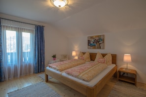 Un dormitorio con una cama de madera, dos mesitas de noche con lámparas, un cuadro en la pared y una ventana con cortinas.