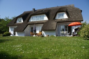 Ein Haus mit Strohdach, weißen Wänden und einer Veranda mit Sitzgelegenheiten.