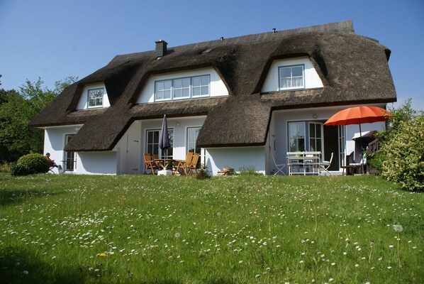 A house with a thatched roof, white walls, and a front porch with outdoor seating. - Holiday house thatched with reed in natural reserve area with garden and terrace (Putbus - Wreechen)