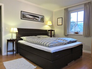 A neatly made bed with striped bedding, two bedside lamps, a framed picture on the wall, and a window with curtains. - Holiday house thatched with reed in natural reserve area with garden and terrace (Putbus - Wreechen)