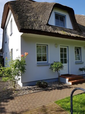 A white house with a thatched roof, two windows, and a small garden with plants and a pathway. - Holiday house thatched with reed in natural reserve area with garden and terrace (Putbus - Wreechen)