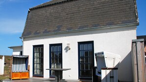 Un edificio bianco con tetto grigio, ampie finestre e una zona patio con tavolo e sedie.