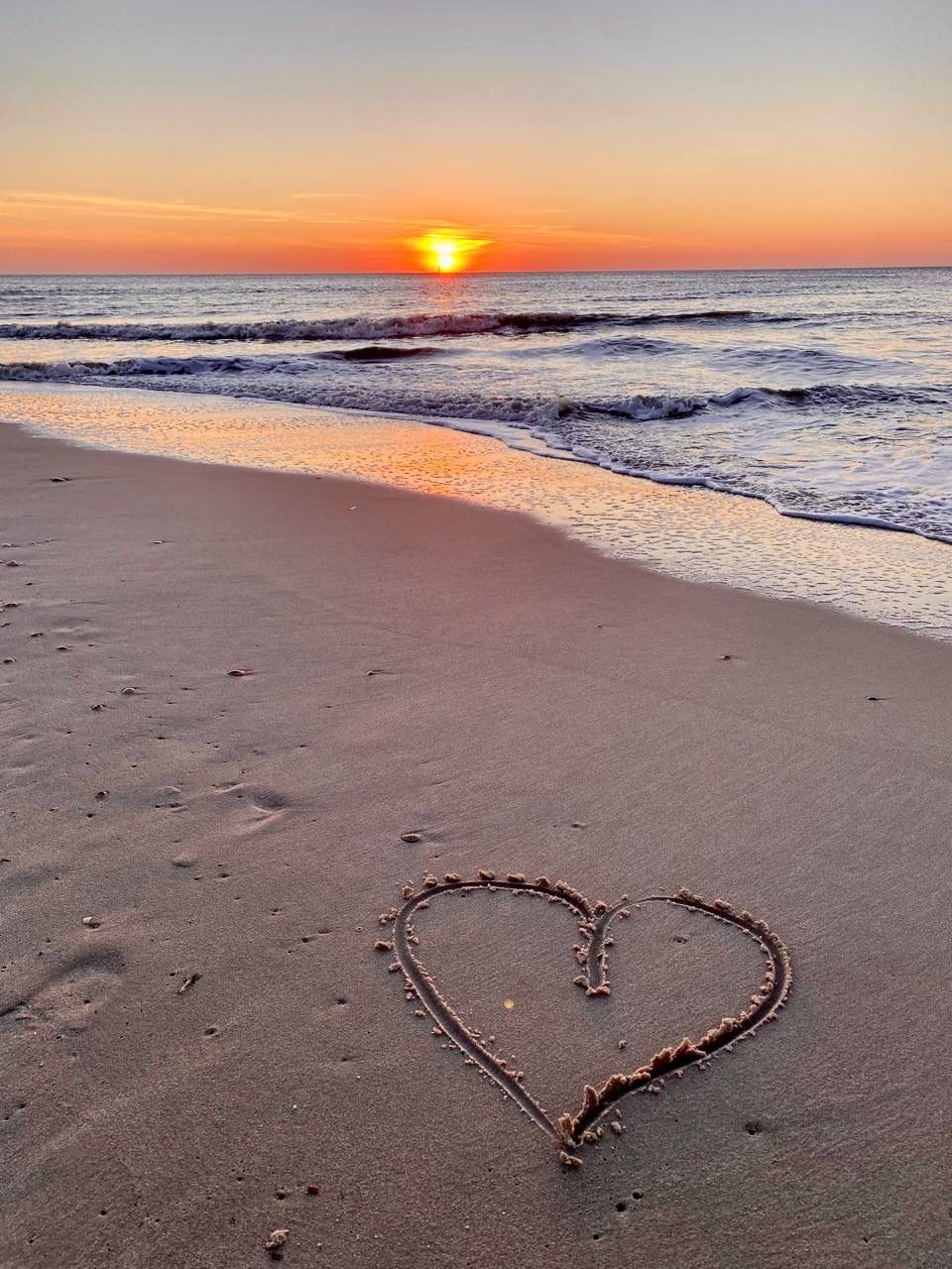 A beach with a heart-shaped drawing in the sand and the ocean in the background.