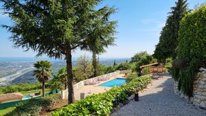 A pool area with a view of a cityscape, surrounded by greenery and a stone wall. - Holiday villa with pool, large terrace and great sea and far view. (Gattières)