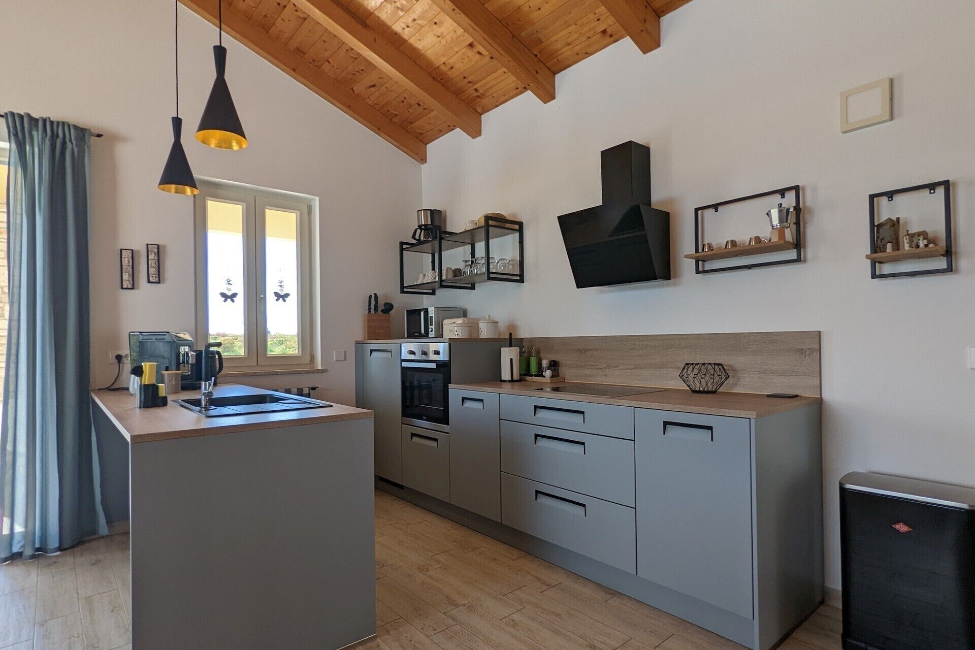 A modern kitchen with a central island, built-in appliances, and a wooden ceiling.