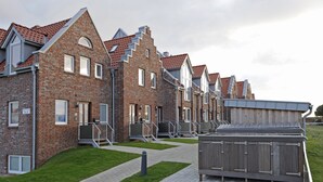 Une rangée de maisons en briques avec des toits à deux versants, un chemin piétonnier pavé et une petite construction en bois.