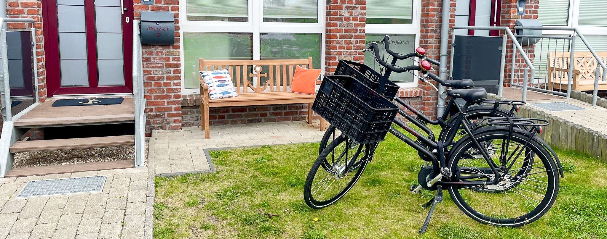 Una bicicleta estacionada frente a un edificio de ladrillo con un banco y una puerta de madera.