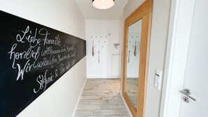 Un couloir avec un tableau noir sur lequel est écrit du texte, un miroir à cadre en bois et une porte dotée d’une poignée.