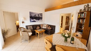 A living room with a sofa, chairs, a coffee table, a bookshelf, and a painting on the wall. - Cozy, sunny & newly renovated apartment with a view of the Zugspitze - 4 stars (Garmisch - Partenkirchen)