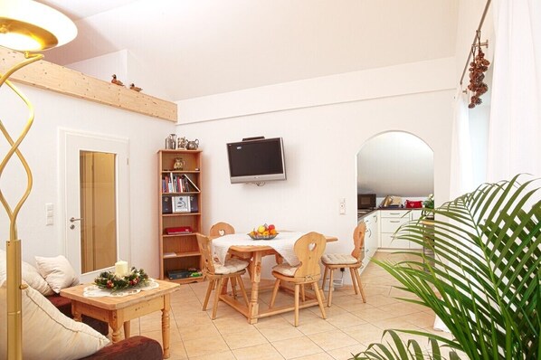 A cozy living room with a wooden dining table, chairs, a TV, and a bookshelf.