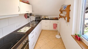 A compact kitchen with white cabinets, a microwave, a stove, and a window with a view. - Cozy, sunny & newly renovated apartment with a view of the Zugspitze - 4 stars (Garmisch - Partenkirchen)