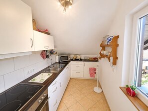 A compact kitchen with white cabinets, a microwave, a stove, and a window with a view.