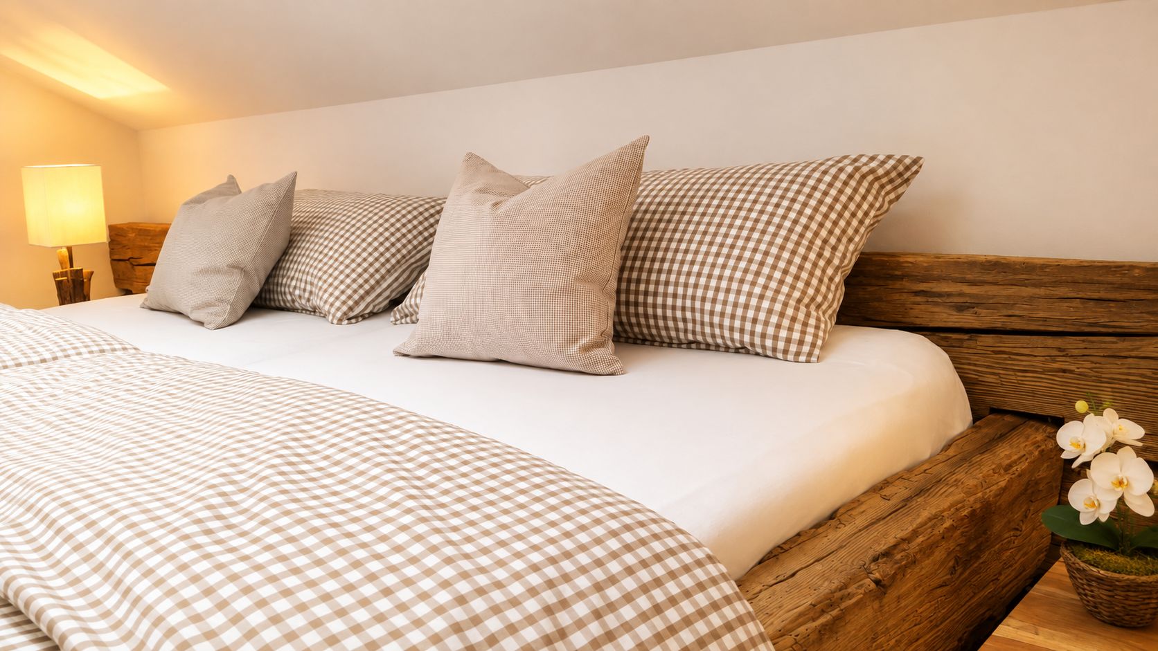A bed with a checkered bedspread and pillows, a wooden headboard, and a nightstand with a lamp.