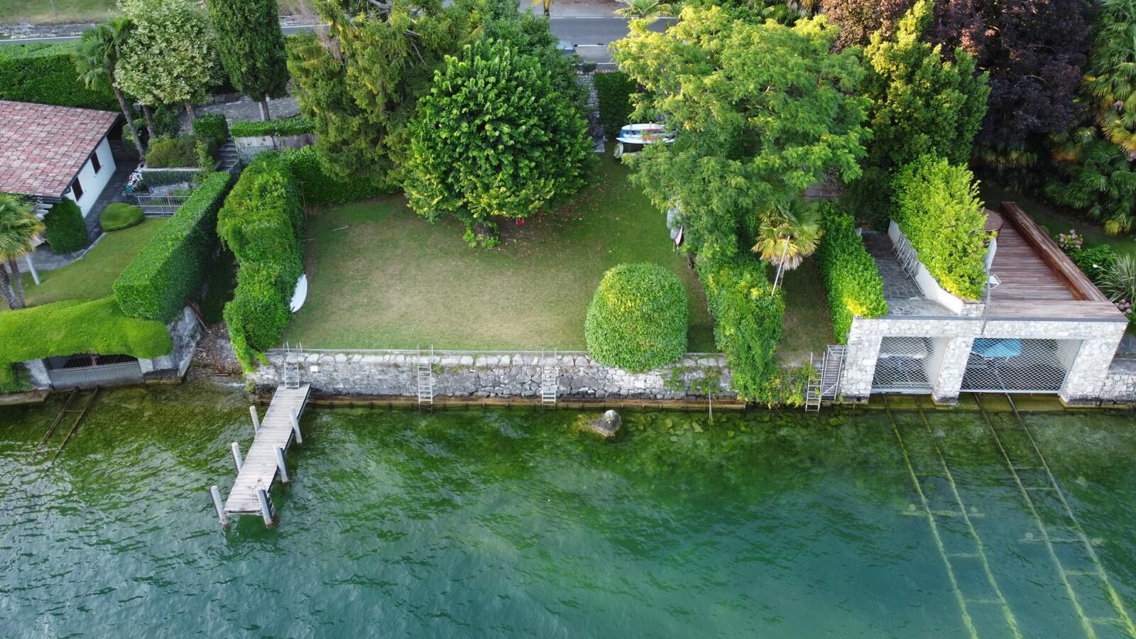 Vue aérienne d’une propriété située au bord de l’eau, avec un quai, une pelouse bien entretenue et divers arbres.