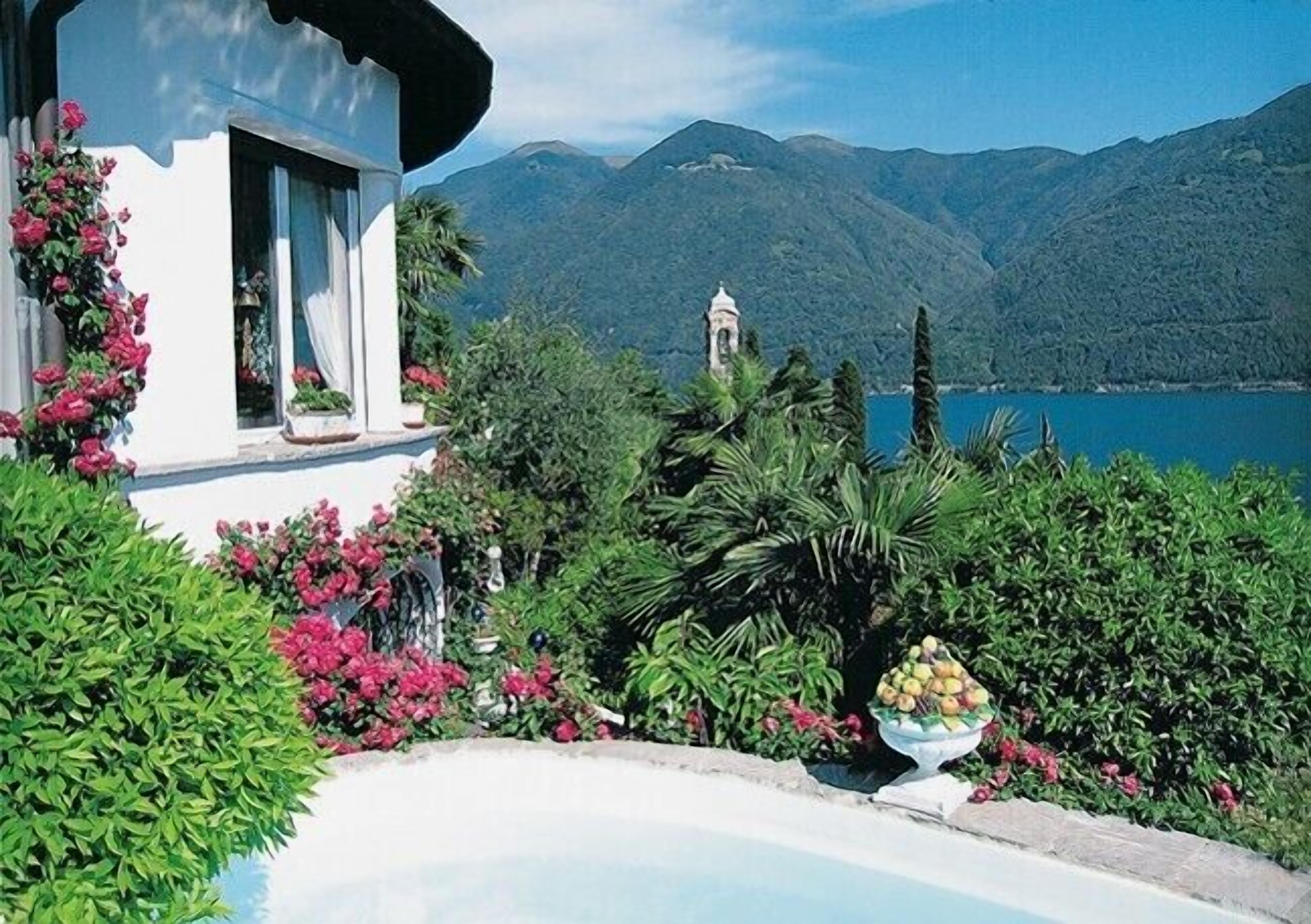 Uma casa com piscina, rodeada por vegetação exuberante e com montanhas ao fundo.