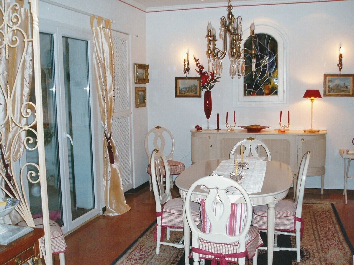 Un coin repas avec une table dressée pour quatre personnes, entourée de chaises blanches agrémentées de touches roses. Un lustre est suspendu au-dessus de la table, et deux lampes murales sont fixées de part et d’autre.