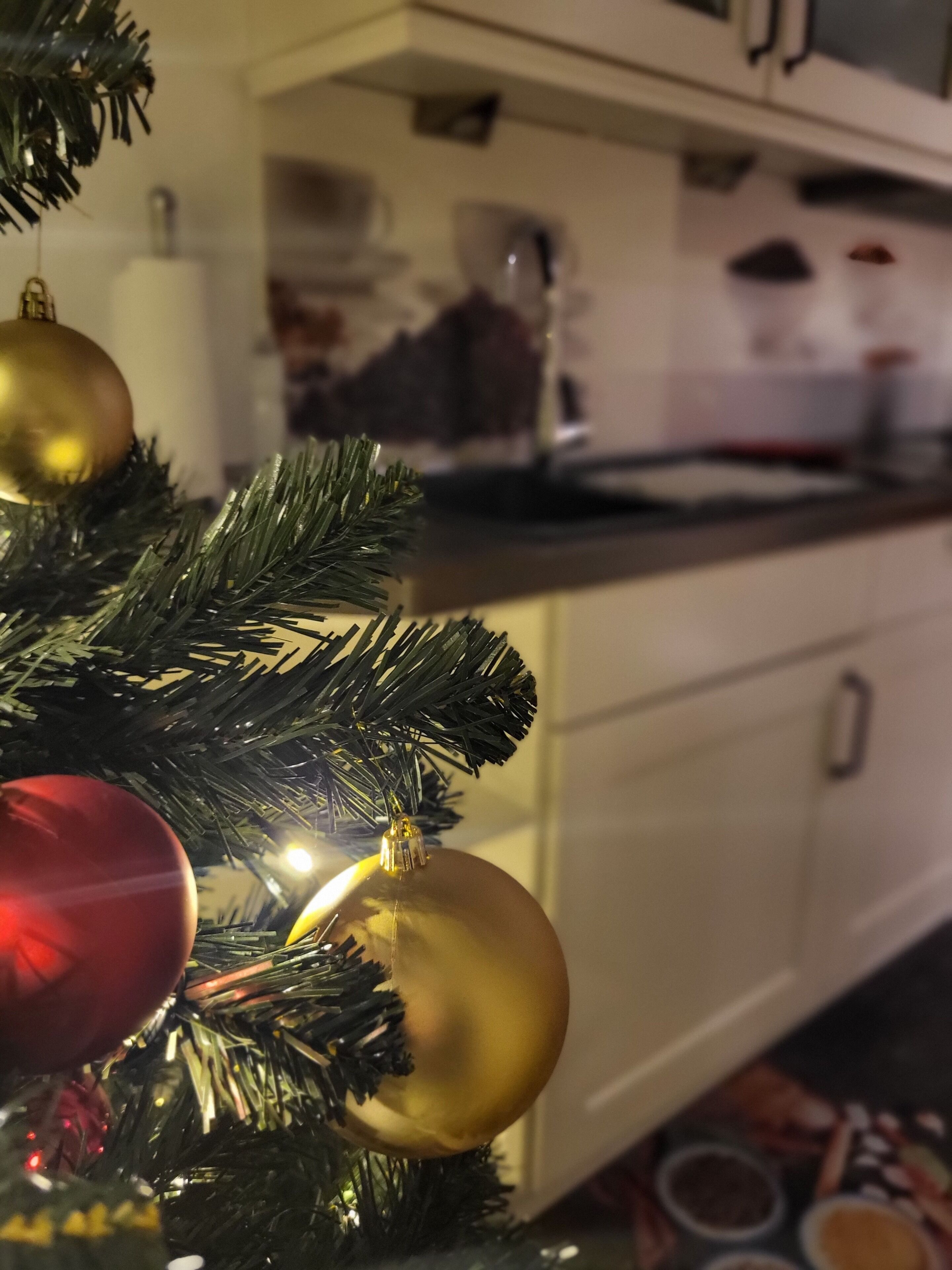 Una cocina con un árbol de Navidad al frente, decorado con adornos dorados y rojos.