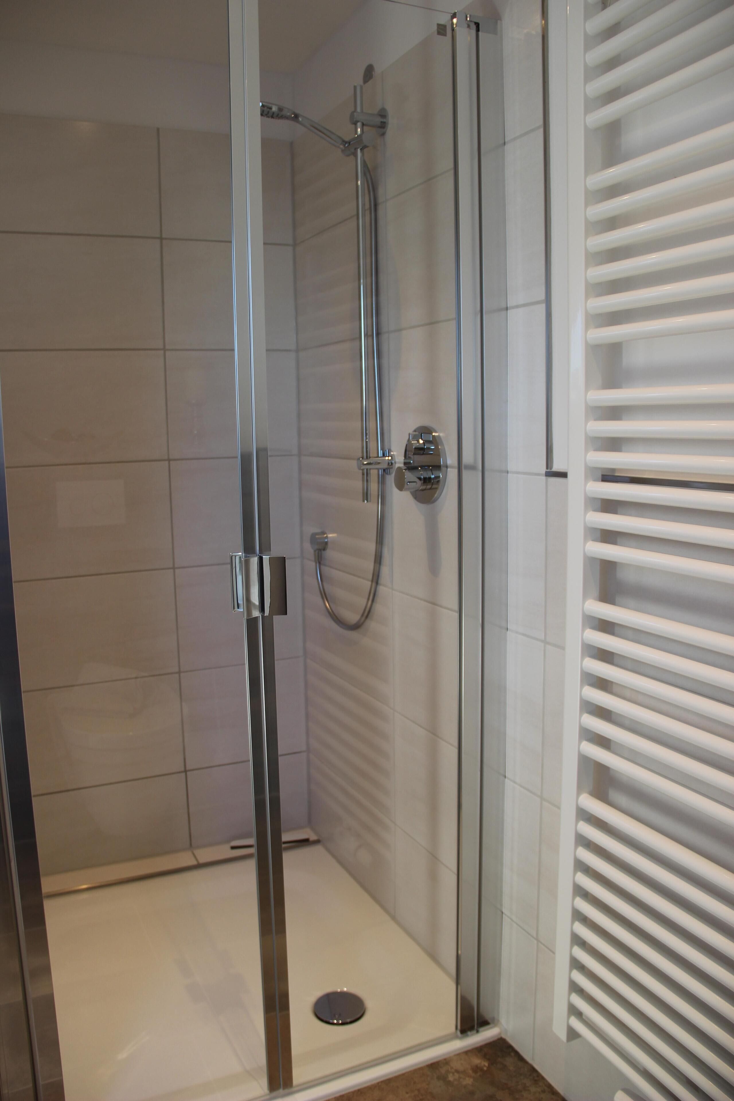 Ducha con cerramiento de vidrio, grifería de cromo y pared de azulejos blancos.