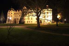 A large, illuminated building with a dome and arched windows, surrounded by a grassy area and trees. - EXCLUSIVE APARTMENT CENTER NOW (Celle)