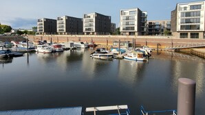 A marina with several boats docked, modern buildings in the background, and a clear sky. - EXCLUSIVE APARTMENT CENTER NOW (Celle)