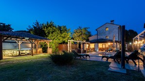 Ein Garten mit einer Pergola, Sitzgelegenheiten im Freien und einem Steinhaus.