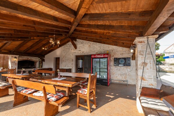 Un espacio de comedor al aire libre con mesas y bancos de madera, un muro de piedra y un refrigerador de Coca-Cola.