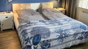 A bedroom with a bed, two bedside tables, a wall with a bird decal, and a window with curtains.