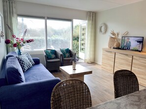 Un salon moderne comprenant un canapé, deux fauteuils, une table basse et un téléviseur posé sur un meuble en bois.