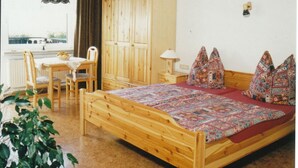 Quarto com cama de madeira, escrivaninha, cadeira, guarda-roupa e janela com cortinas.
