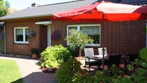 Une maison en briques avec un patio, un parasol rouge et une table avec des chaises.