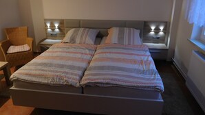 Une chambre avec un grand lit, deux tables de chevet avec des lampes, une chaise et deux tableaux accrochés au mur.