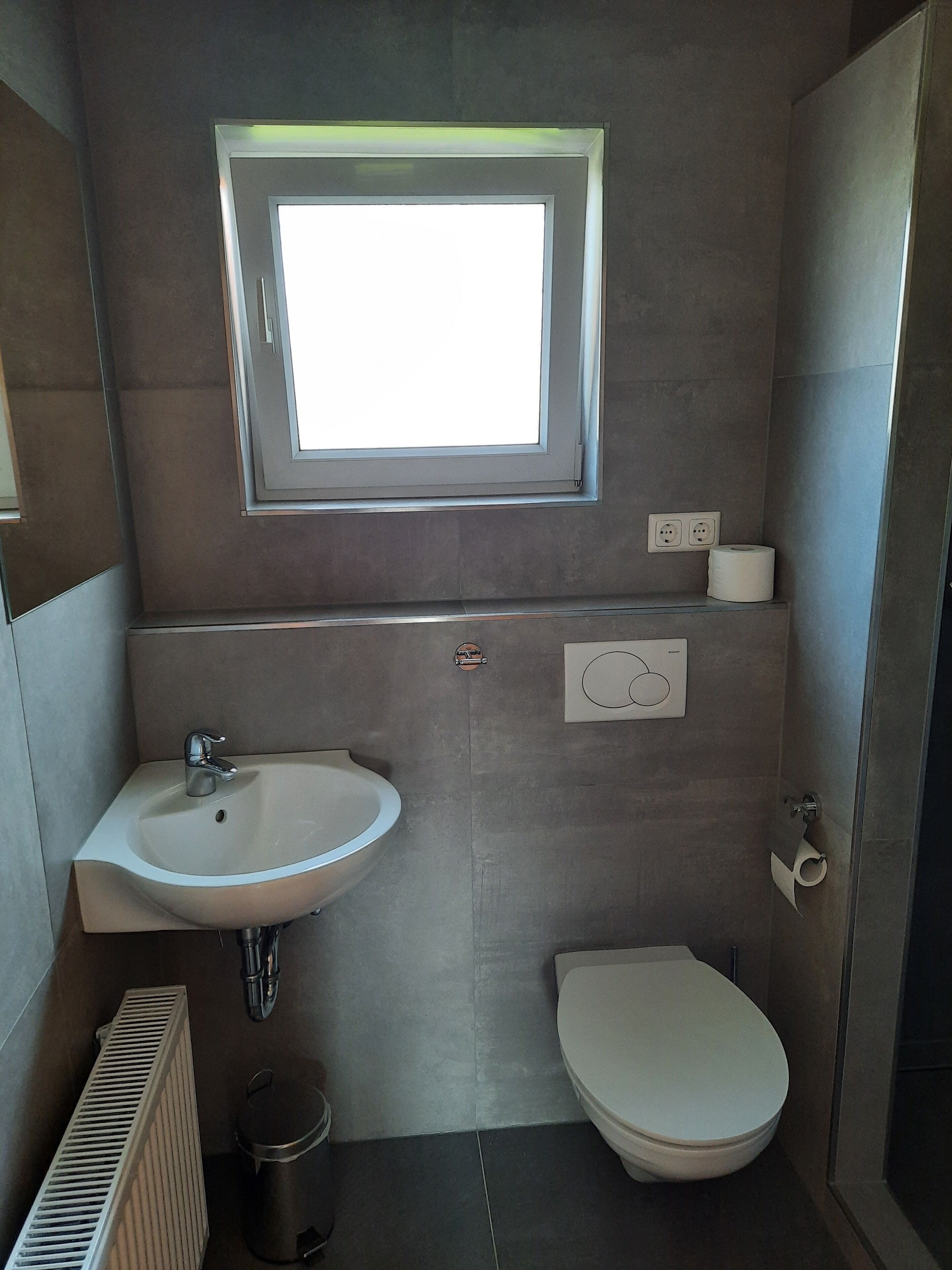 A modern bathroom with a window, a sink, a toilet, and a radiator.