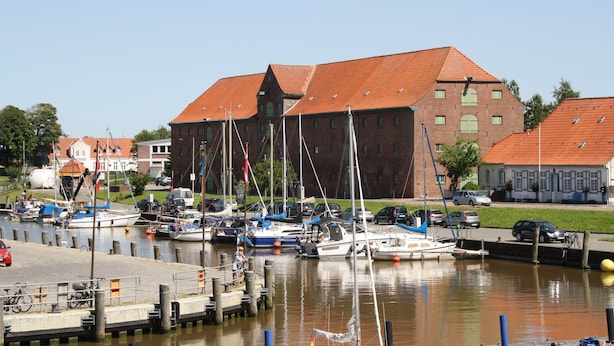 Un port de plaisance avec des bateaux amarrés, un bâtiment en briques avec un toit rouge et un ciel dégagé.