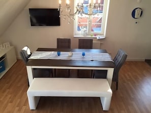 A dining area with a rectangular table, bench, and chairs. A chandelier hangs above the table. - Bright & modern, 4-star apartment for up to 5-6 people (maisonette) (Langeoog)