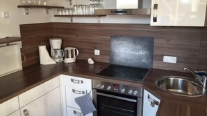 A modern kitchen with a built-in oven, a coffee maker, and a kettle. There are wine glasses on a shelf above the counter. - Bright & modern, 4-star apartment for up to 5-6 people (maisonette) (Langeoog)