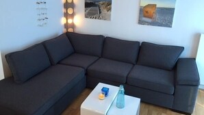 A modern living room with a dark grey sectional sofa, a white coffee table, and three framed pictures on the wall. - Bright & modern, 4-star apartment for up to 5-6 people (maisonette) (Langeoog)