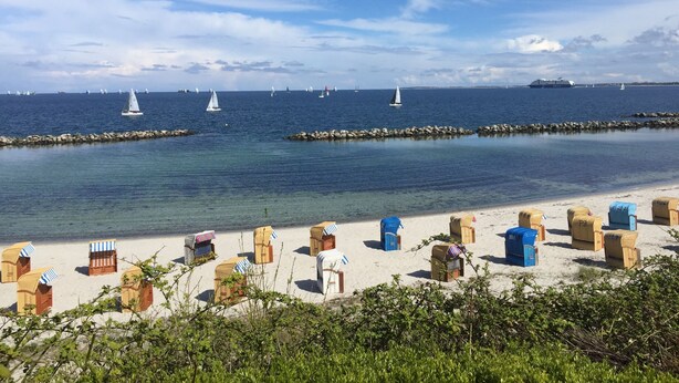 A beach with rows of beach huts and a rocky breakwater. - Beach and sea(h)r in a vacation home with garden close to the beach at Schilksee⛵️ (KI)