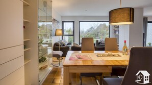A modern dining area with a wooden table, chairs, and a hanging lamp. - Beach and sea(h)r in a vacation home with garden close to the beach at Schilksee⛵️ (KI)