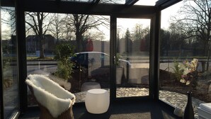A modern room with a glass wall, a white furry chair, a white ottoman, and a potted plant. - Beach and sea(h)r in a vacation home with garden close to the beach at Schilksee⛵️ (KI)