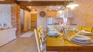 Zona de menjador amb taula de fusta preparada per a sis, envoltada de cadires, ubicada en una habitació amb parets de maó descobert i viges de fusta.