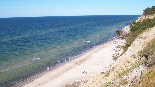 Une plage avec une eau d’un bleu limpide, un rivage sablonneux et une falaise rocheuse.