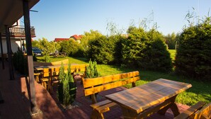 Un espace patio aménagé avec des bancs en bois et des tables de pique-nique, entouré de verdure et offrant une vue sur une maison en arrière-plan.