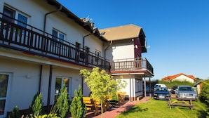 Un immeuble de deux étages doté d’un balcon, d’une terrasse et de voitures garées.