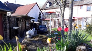 A garden with various plants and flowers, a stone bench, and a car parked in front of a building with a red roof. - Take a few days blue, in the holiday home Blue (Berlingen)