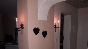 A hallway with two black heart-shaped decorations hanging on the wall, a lit candle on the left, and a white ceiling. - Take a few days blue, in the holiday home Blue (Berlingen)