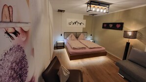 A bedroom with a bed, a bedside table, a lamp, and a wall with a mountain design and heart decorations. - Vacation apartments Unterluimes (Telfes im Stubai)
