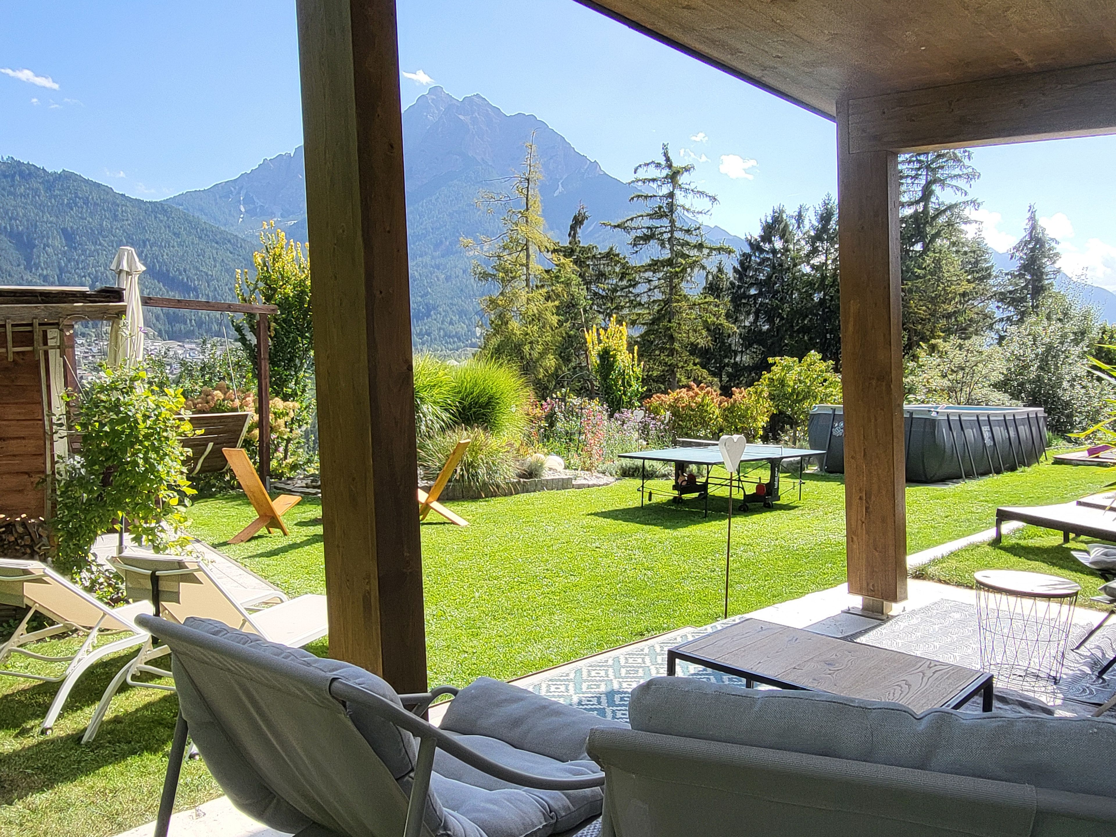A covered outdoor area with a table and chairs, a ping pong table, and a view of mountains.