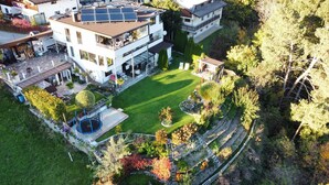 A modern two-story house with a rooftop solar panel array, a well-maintained lawn, and a small trampoline. - Vacation apartments Unterluimes (Telfes im Stubai)